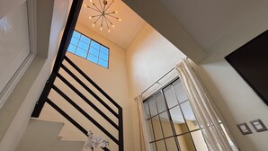 Un escalier avec des rampes noires menant à un palier doté d’une grande fenêtre et d’un luminaire décoratif au plafond.