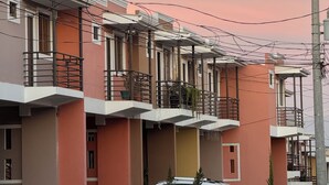 Une rangée d’immeubles résidentiels modernes à plusieurs étages, dotés de balcons, avec une voiture blanche garée et des plantes en pot.