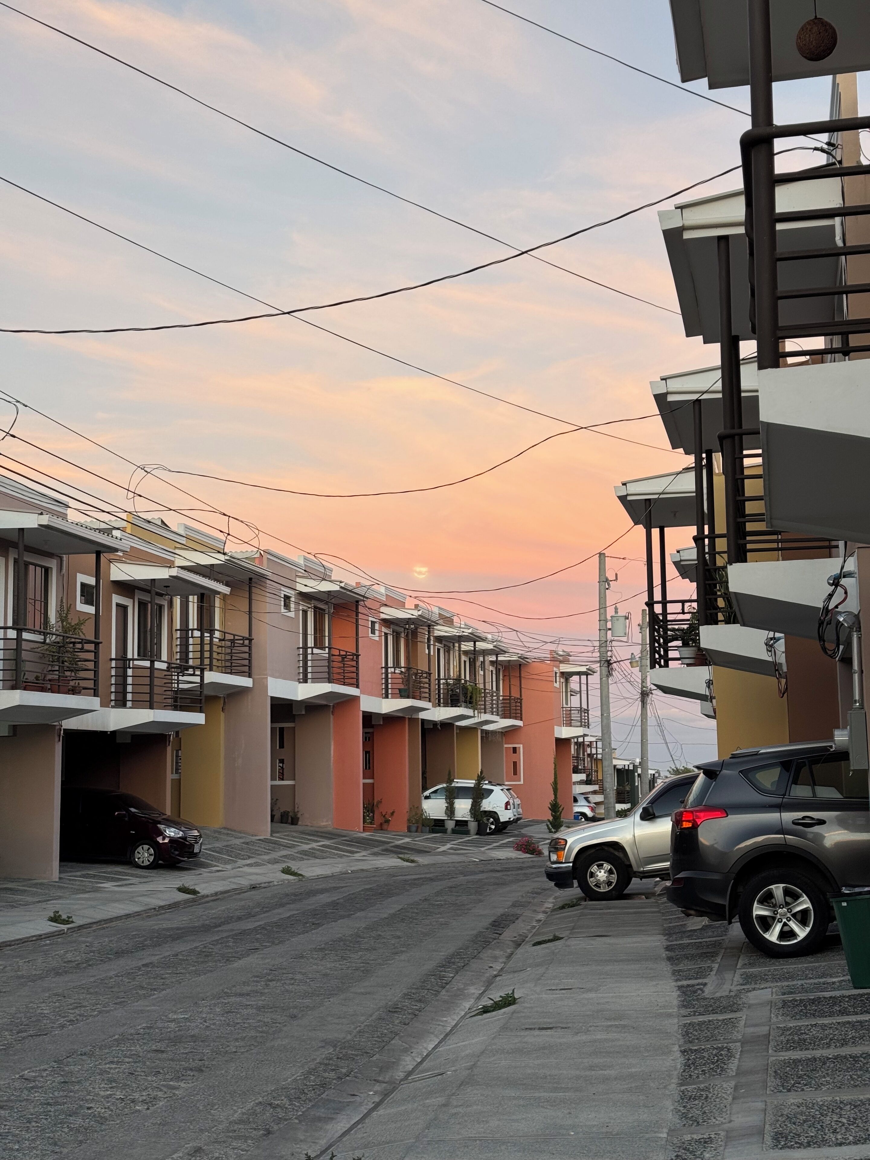 Un carrer residencial amb edificis d'altes plantes, cotxes aparcats i línies elèctriques a la vista.