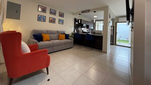 Un salon moderne avec un canapé gris, un fauteuil rouge et un coin cuisine doté de tabourets de bar.