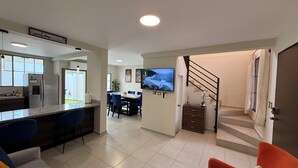 Un salon moderne comprenant un espace cuisine, un coin repas et un escalier menant à l’étage supérieur.