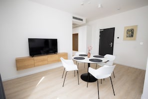 A modern room with a flat-screen TV, a round dining table with chairs, and a wooden cabinet. - Kula & the Top Apartments (Zagreb)