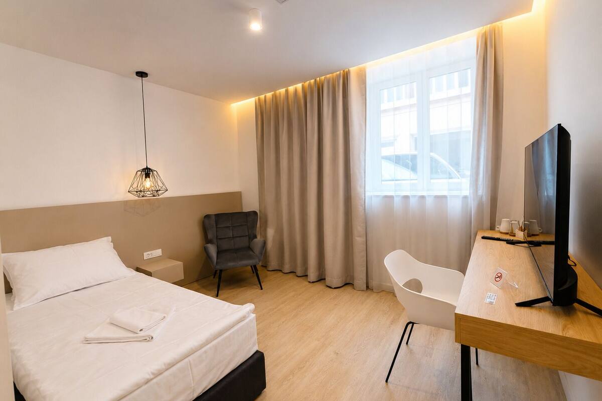 Una habitación de hotel con cama, escritorio, silla, televisor y ventana con cortinas.