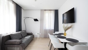 Un salon moderne comprenant un canapé, une table à manger avec des chaises, un téléviseur à écran plat fixé au mur et une lampe sur pied.