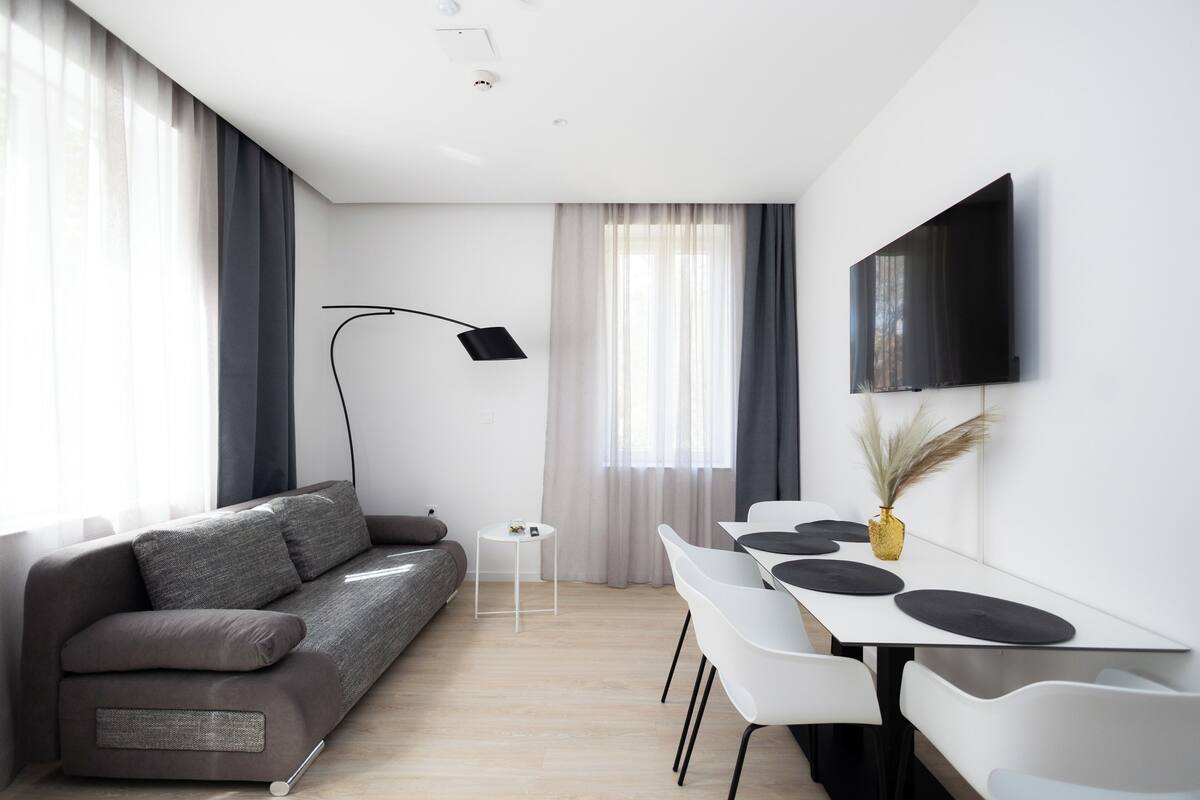 Una sala de estar moderna con un sofá, una mesa de comedor con sillas, un televisor de pantalla plana en la pared y una lámpara de pie.