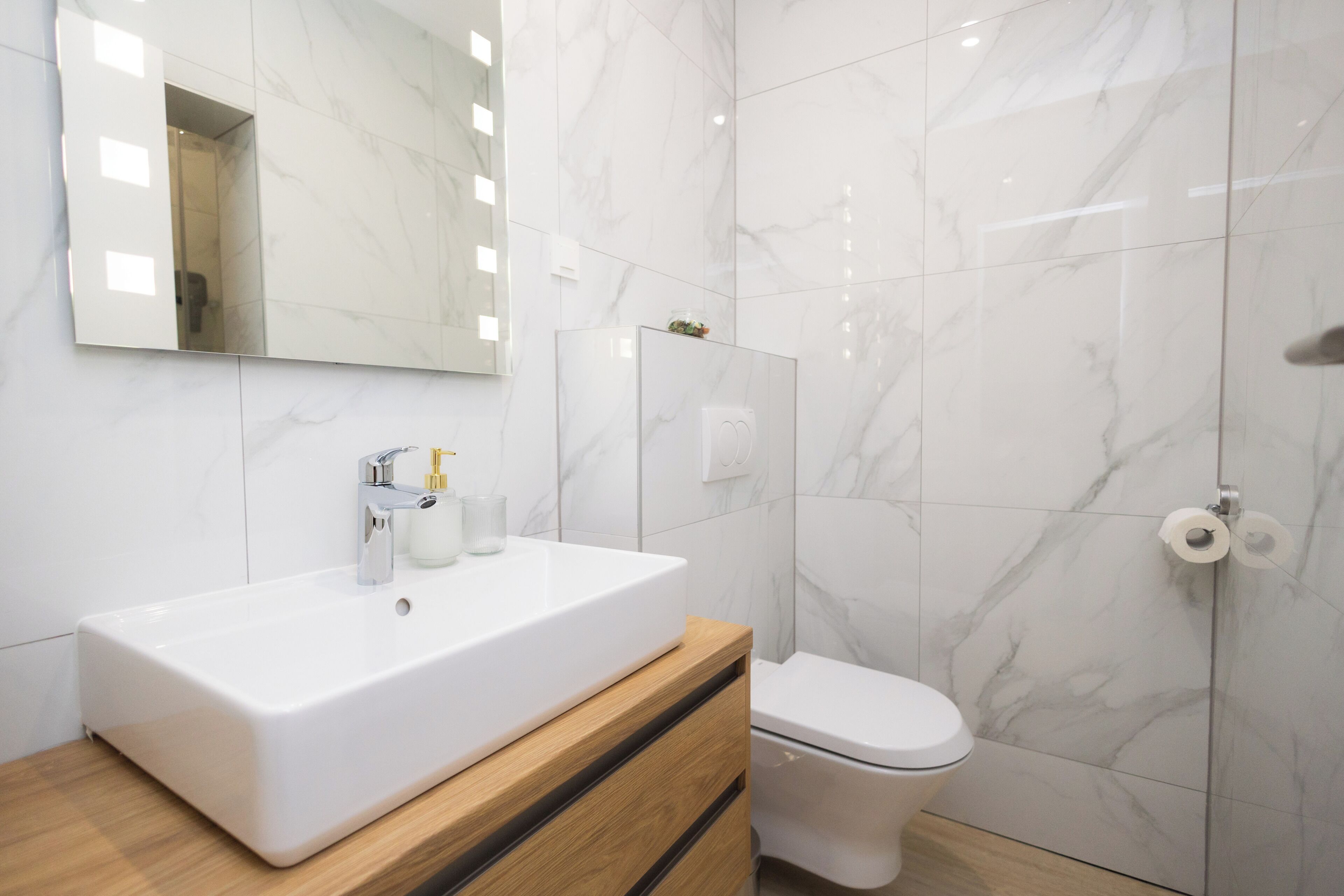 A modern bathroom with a white sink, wooden cabinet, and a toilet.