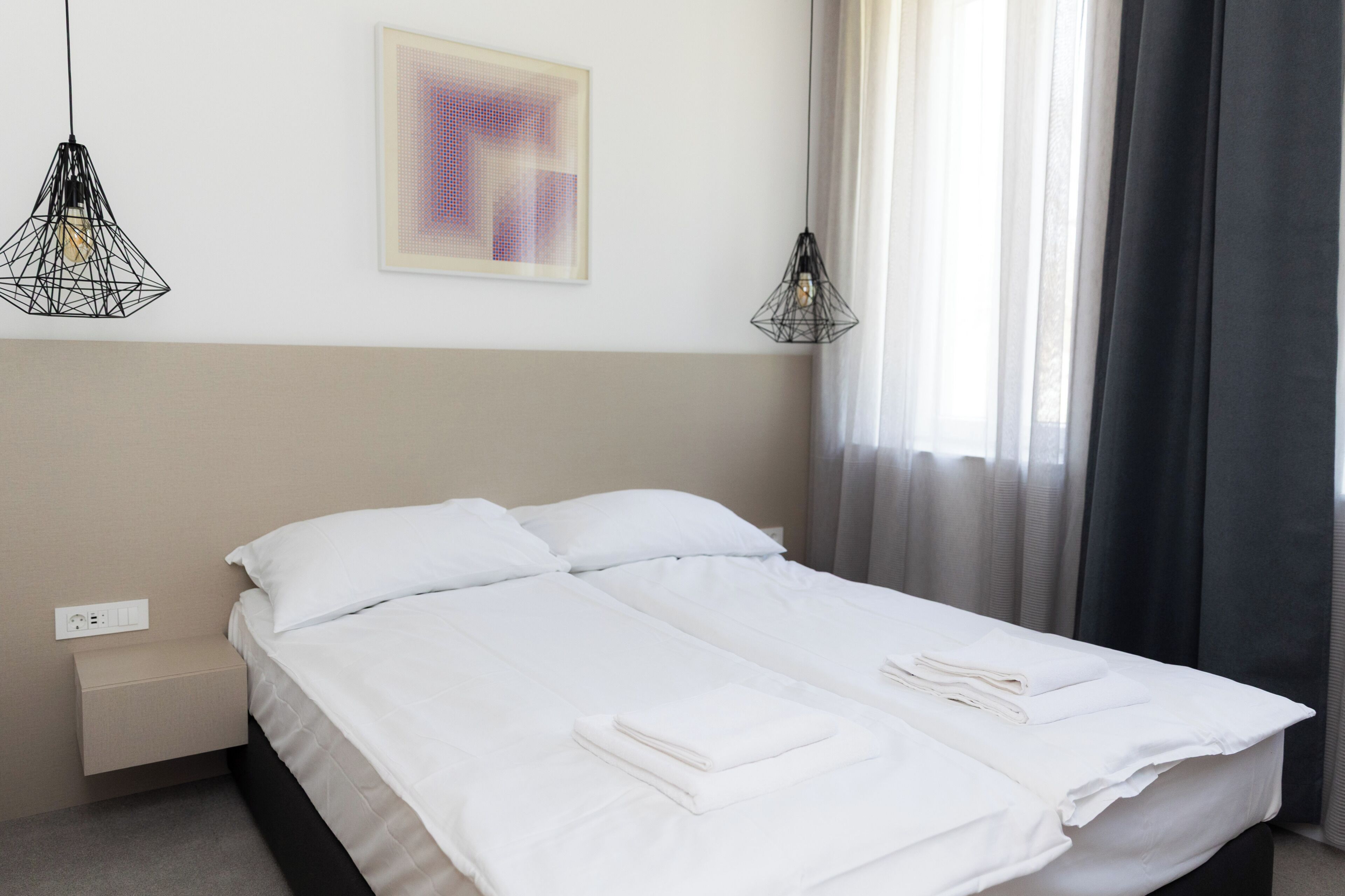 Una camera d'albergo con un letto, due comodini, una presa di corrente, un'opera d'arte astratta incorniciata e due lampade a sospensione.