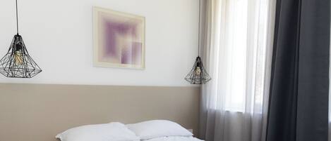 Una camera d'albergo con un letto, due comodini, una presa di corrente, un'opera d'arte astratta incorniciata e due lampade a sospensione.