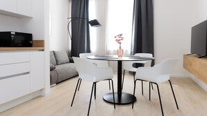 Un salon moderne avec une table à manger ronde, des chaises blanches, un canapé, un téléviseur posé sur un meuble en bois et un lampadaire.