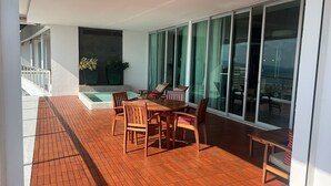 A sunlit balcony with a wooden table and chairs, a small pool, and large sliding glass doors.