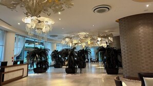 A spacious lobby with multiple chandeliers, large potted plants, and a reception desk.