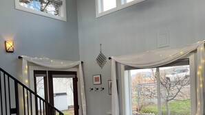 Un vaste salon doté d’un haut plafond, d’un ventilateur de plafond, d’une grande fenêtre offrant une vue sur l’extérieur, d’un canapé blanc, de deux fauteuils à motifs et d’un tapis à motifs.