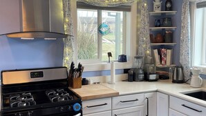 Une cuisine moderne avec des meubles blancs, une cuisinière en acier inoxydable et une fenêtre avec des rideaux.