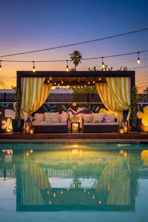 A poolside lounge with a sofa, cushions, and ambient lighting. - Iconic Vegas Villa : Heated Pool| Movie Room (Las Vegas)