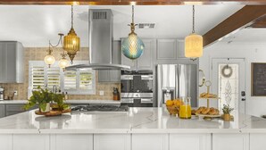 A modern kitchen with a large island, stainless steel appliances, hanging pendant lights, and a breakfast bar.