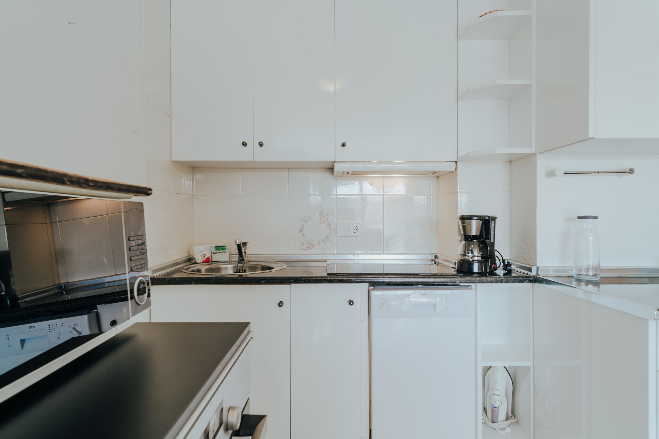 Une cuisine moderne avec des meubles blancs, un plan de travail noir, une machine à café et un lave-vaisselle.
