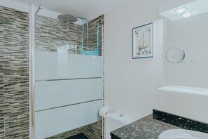 Une salle de bain moderne avec une douche à l’italienne en verre, un lavabo doté d’un plan de toilette noir et un tableau encadré au mur.