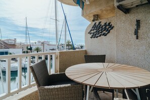 Un balcon agrémenté de fauteuils en osier et d’une table ronde, offrant une vue sur une marina avec des bateaux et un ciel dégagé.
