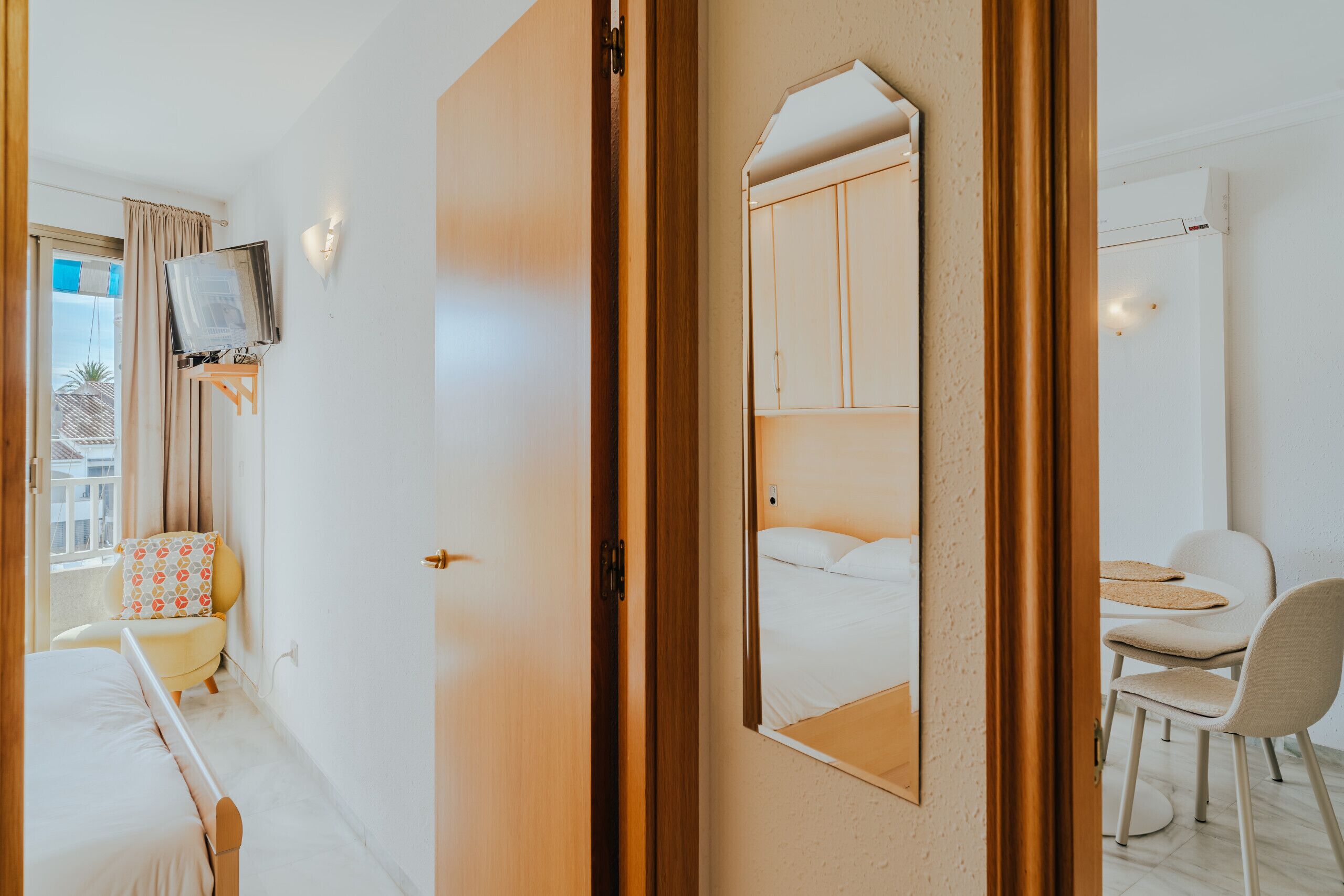 Une chambre d’hôtel avec un lit, un bureau, une chaise, un téléviseur posé sur un meuble et un grand miroir.
