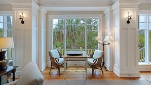 Ein Zimmer mit einem großen Fenster, zwei Korbstühlen, einem Tisch und einer Lampe.