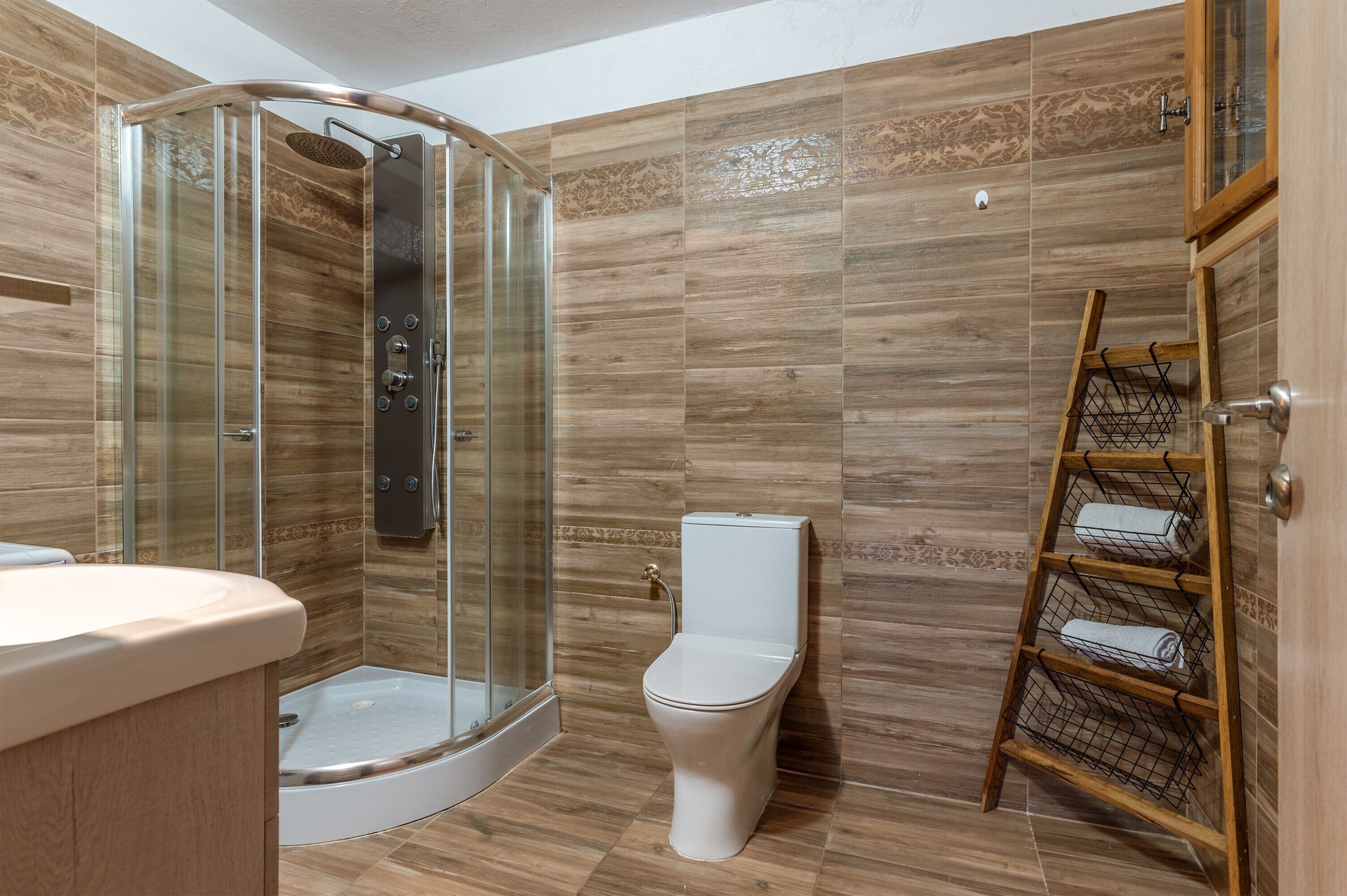 Een badkamer met een douche met glazen wand, een toilet en een houten handdoekhouder.