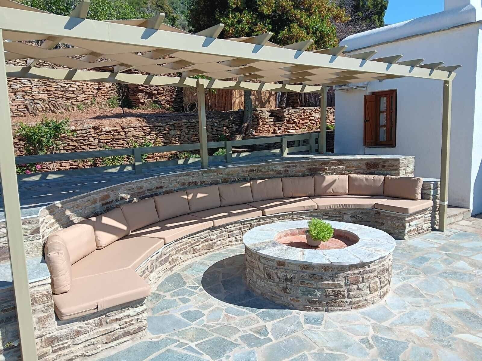 A stone-tiled outdoor seating area with a curved sofa and a circular stone fire pit.
