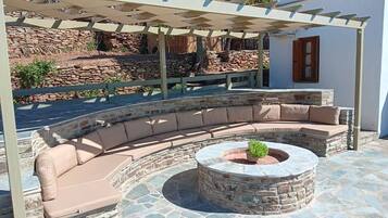 A stone-tiled outdoor seating area with a curved sofa and a circular stone fire pit.