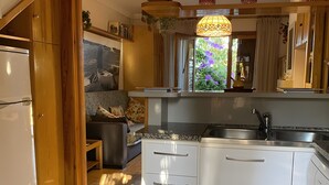 Ett kompakt kök med vita skåp, en diskho i rostfritt stål och en matplats med en soffa och ett bord.