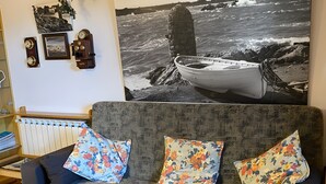 Ett vardagsrum med en grå soffa, blommiga kuddar, en väggklocka och ett inramat fotografi.