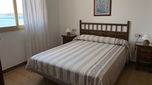 A neatly made bed with a striped bedspread, a wooden headboard, and a nightstand with a lamp. - Apartment 'Platja Mar 2' with Sea View and Balcony (L'Escala)