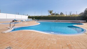 A swimming pool with a tiled deck, lounge chairs, and a metal ladder.