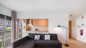 A modern living room with a grey sectional sofa, a floor lamp, and a view of the kitchen through an open door.