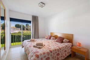 Ein Schlafzimmer mit einem großen Bett, einem Nachttisch, einer Lampe und Blick auf eine grüne Landschaft durch ein Fenster.