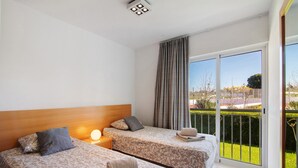 A hotel room with two beds, a nightstand, a lamp, a window with curtains, and a view of the outside.