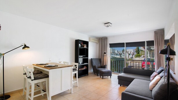 A living room with a sofa, a dining table with chairs, a bookshelf, and a balcony with a view.