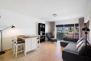 Ein Wohnzimmer mit einer Couch, einem Esstisch mit Stühlen, einem Bücherregal und einem Balkon mit Blick.