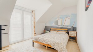 A bedroom with a sloped ceiling, a bed, a nightstand, a dresser, and a sailboat mural on the wall.