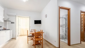 A modern kitchen with white cabinets, a dining area with wooden chairs, a TV mounted on the wall, and a glass shower enclosure. - Holiday Home 'Diga' with Mountain View, Wi-Fi and Air Conditioning (Palermo)