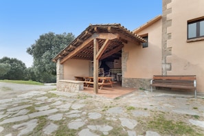 Un bâtiment en pierre agrémenté d’une pergola en bois, d’un banc et d’une table de pique-nique.