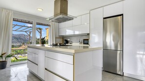 A modern kitchen with a large island, stainless steel appliances, and a view of mountains through the window.