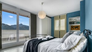 A bedroom with a bed, a view of mountains, a sliding glass door, and a shelf with books and decorative items.