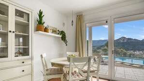 A dining area with a table and chairs, a cabinet with glass doors, and a view of a mountain and pool through a glass door.