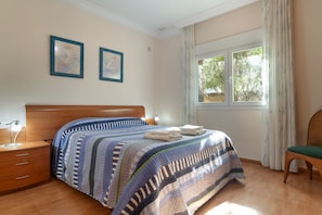 A bedroom with a bed, a chair, a nightstand, and a window with curtains.