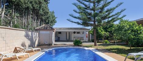 A swimming pool with lounge chairs, a building with a tiled roof, and surrounding trees.