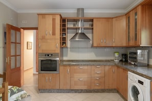 A kitchen with wooden cabinets, a stainless steel range hood, a built-in oven, a washing machine, and a coffee maker.