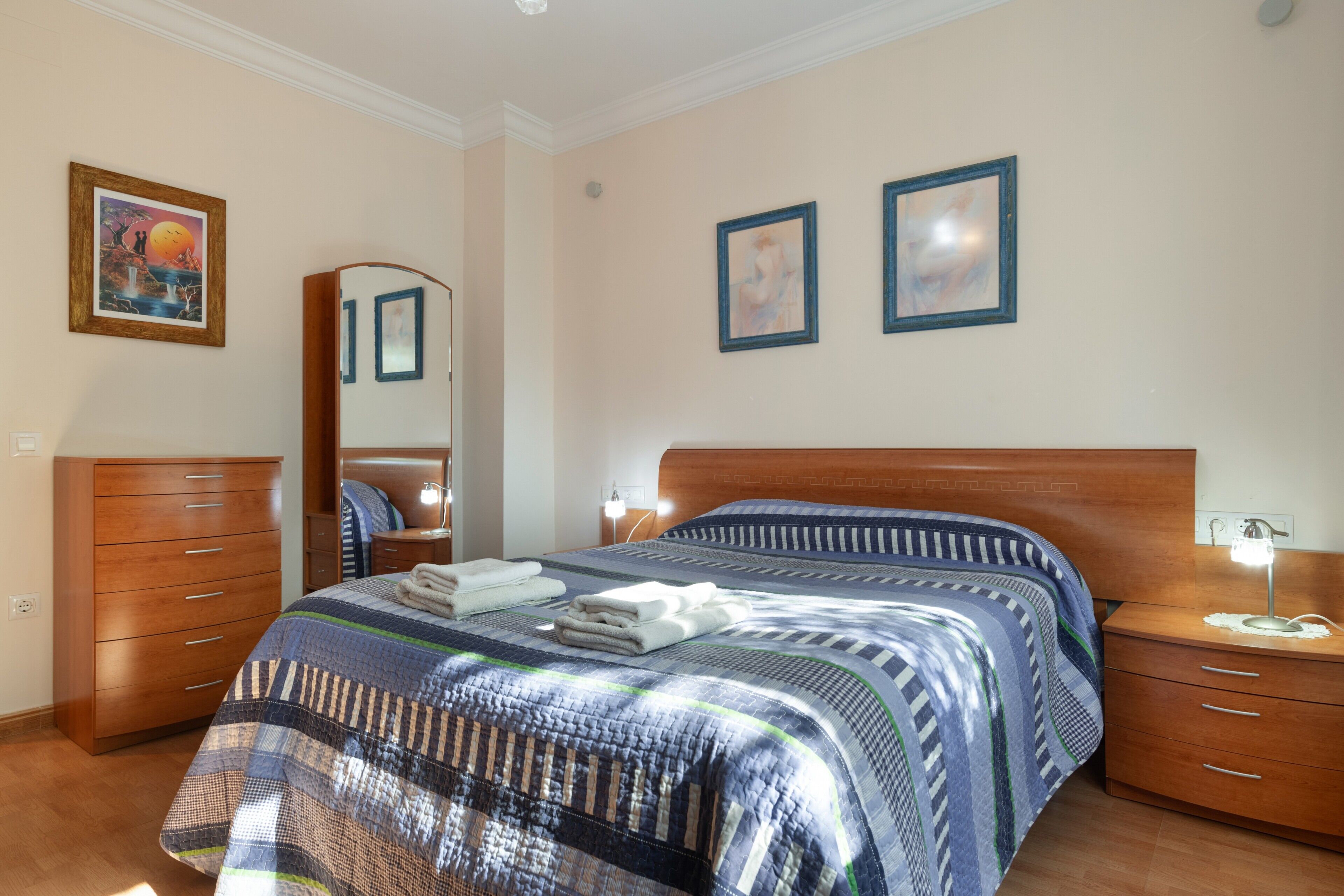 A bedroom with a bed, a dresser, a nightstand, and two framed pictures on the wall.