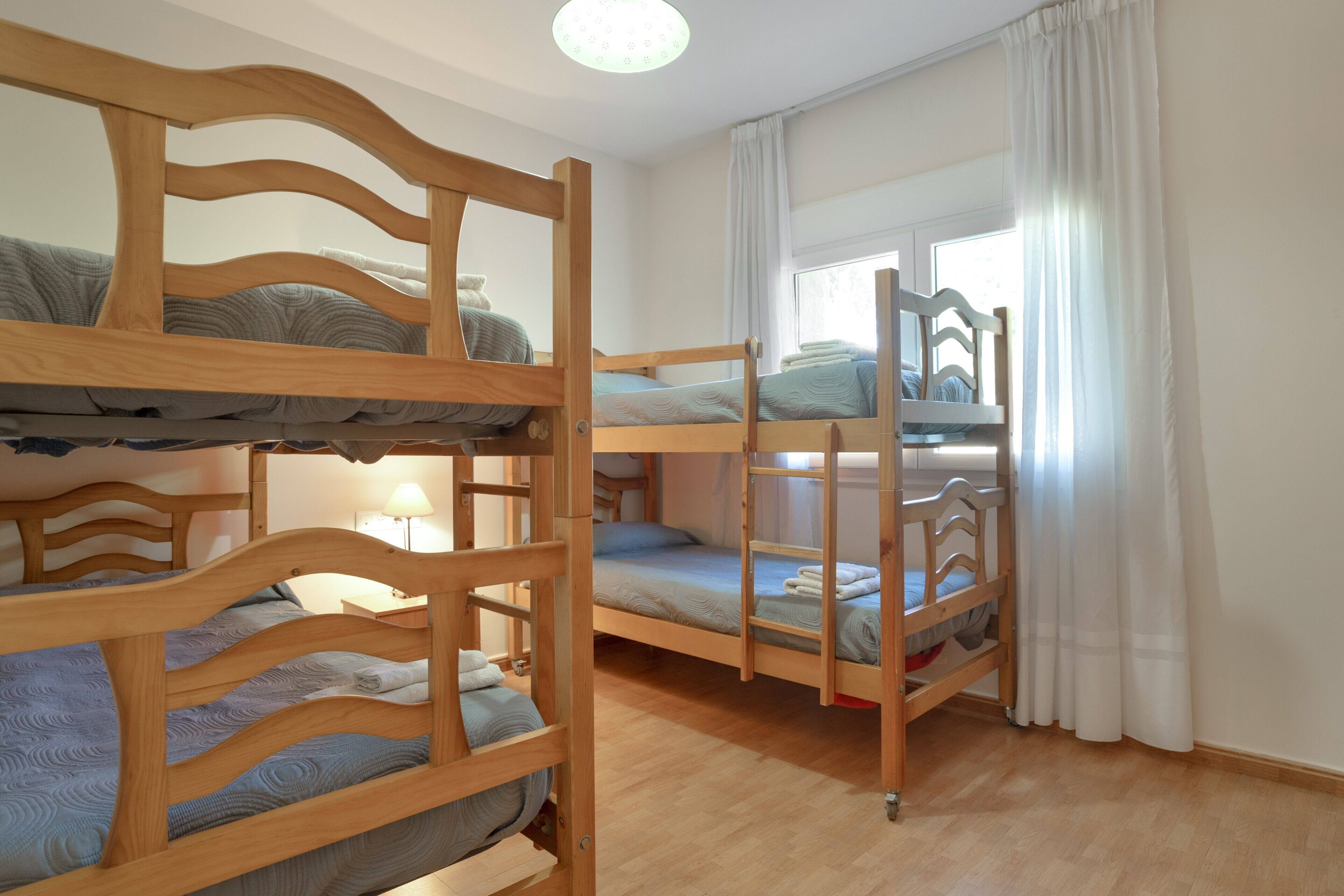 A room with bunk beds, a bedside table, a lamp, and a window with curtains.