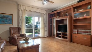 Ein Wohnzimmer mit braunem Ledersofa, einem Holztisch, einem Deckenventilator und einem Fernseher auf einem Holzständer.