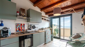 Una cocina con estufa, horno y lavadero, un comedor con una silla, y un balcón con vistas.