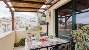 Terraza en la azotea con una mesa lista para comer, rodeada de sillas y vistas a un paisaje urbano.